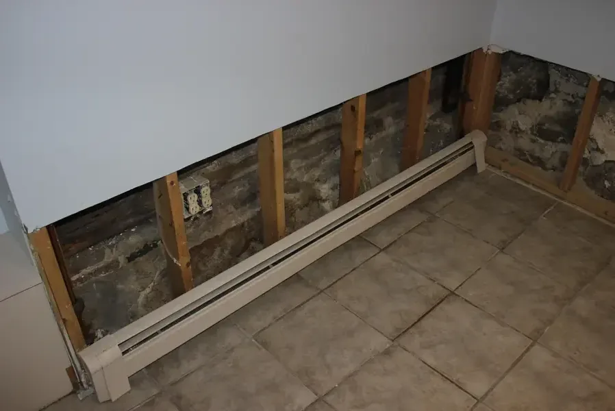 Wet drywall cut away above a baseboard heater to expose the damp wall cavity