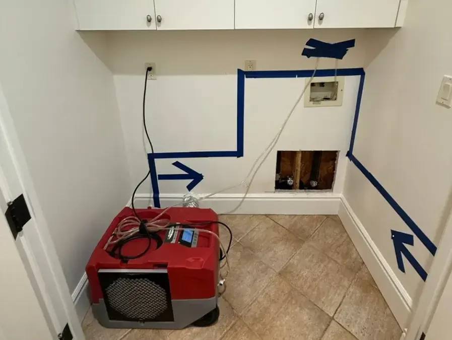 Blue tape marking the mapped wet area on a laundry wall while a dehumidifier dries it