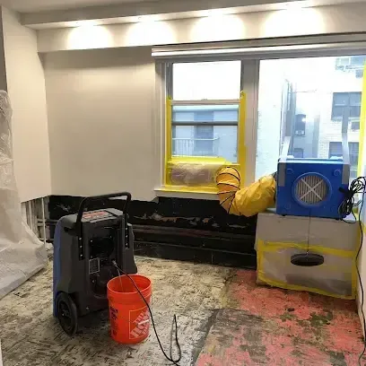 A dehumidifier and air mover running beside an opened wall in a home drying after water damage