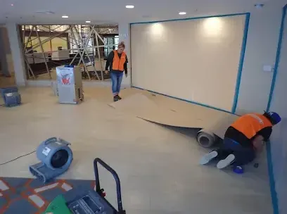 A crew pulling up wet flooring in a commercial space while an air mover runs